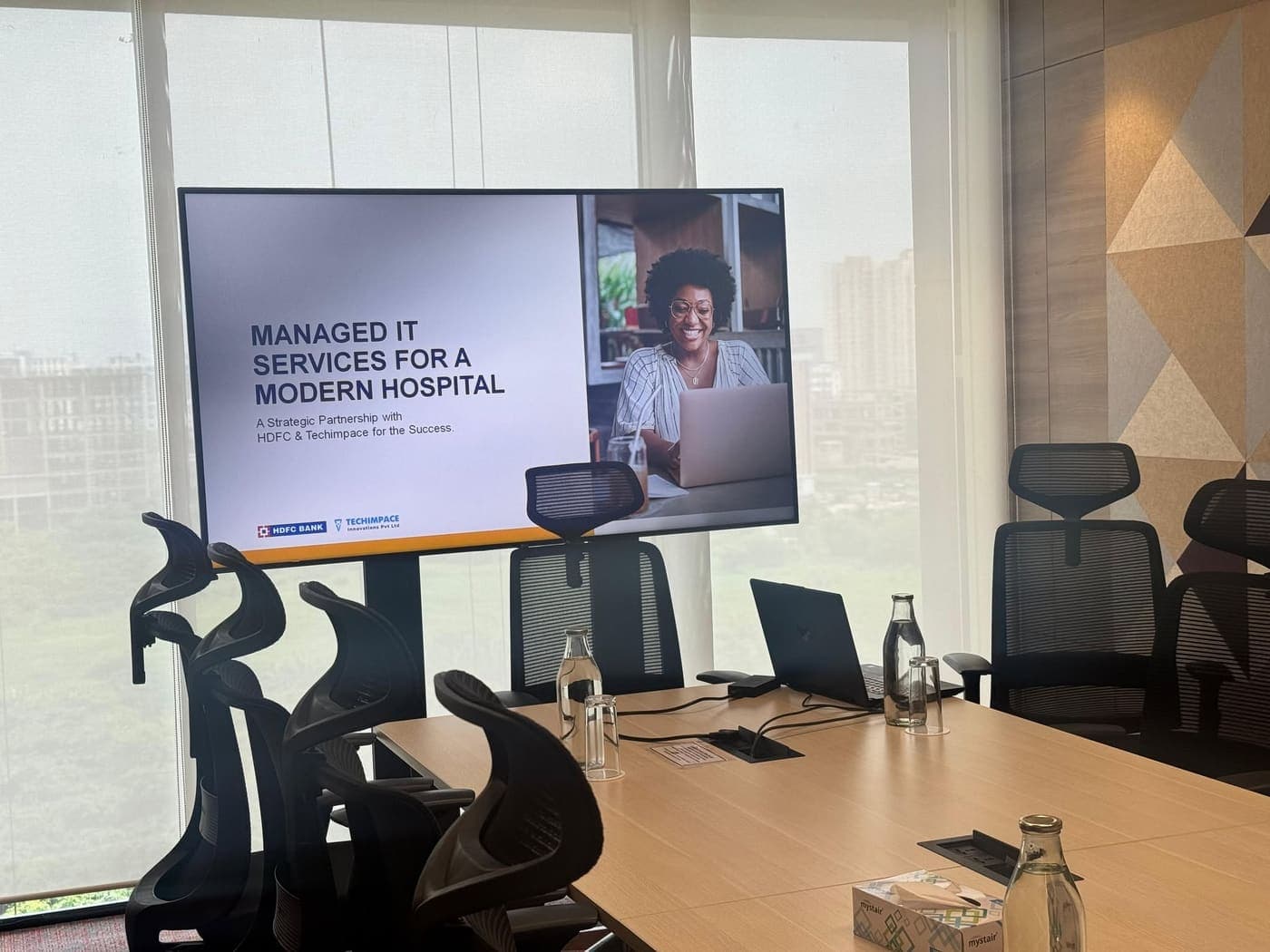 Boardroom with a wall-mounted screen showing a Techimpace and HDFC Bank managed IT services presentation